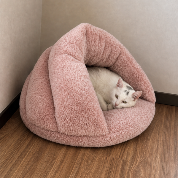 White cat resting inside a pink plush slipper-style cat bed tucked into a quiet corner -- a warm cosy corner as part of an indoor cat enrichment routine